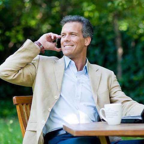 A businessman sitting outdoors talking on a mobile phone.